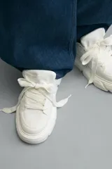 Zapatilla urbana de color blanco con diseño de suela gruesa con volumen y textura irregular. Presenta un corte superior con paneles combinados y cierre mediante cordones al tono.