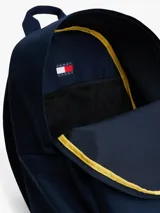 Mochila de diseño redondeado color azul marino, con asa superior, correas ajustables y acolchadas. Presenta un compartimento principal con cierre, bolsillo exterior con cremallera y parche con el logo de Tommy Jeans en la parte delantera.