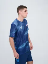 Remera de entrenamiento Umbro del Club Nacional de Football, modelo Press, para hombre. Diseño en tonos de rojo con patrón estampado tipo humo o abstracto, cuello redondo y mangas cortas. Incluye el logo de Umbro y el escudo del club en el pecho.