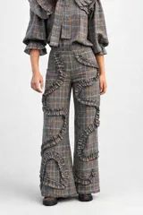 Pantalón de tiro alto con corte recto y diseño de cuadros en tonos grises y naranjas. Presenta detalles de volados aplicados en forma sinuosa a lo largo de las piernas.