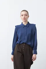 Camisa negra de estilo sastrero con cuello clásico, frente abotonado y mangas largas con puños ajustados. Presenta un diseño con hombreras sutiles que aportan estructura a la prenda.