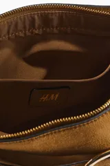 Cartera de hombro color tostado con acabado de gamuza, correa ajustable y tira decorativa frontal con hebilla metálica dorada.