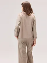 Camisa de manga larga con diseño bicolor en tonos tierra. Presenta un panel frontal y trasero en color beige, contrastado con mangas de un tono marrón más oscuro y textura satinada. Posee cuello redondo y corte recto.
