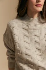 Sweater de punto color beige con diseño geométrico en relieve, cuello alto y mangas largas con puños acanalados.
