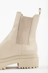 Bota tipo chelsea con suela track de goma en color marrón y capellada de cuero negro. Presenta elásticos laterales y tirador trasero.
