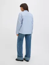 Camisa de manga larga con cuello clásico y cierre frontal de botones. Presenta un diseño a rayas verticales en tonos celestes y blancos, con puños anchos y un corte relajado.