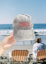 Gorro de visera de tela color gris desgastado, con bordado frontal en hilo rojo que dice "COSTA DULCE" y un diseño de ondas o símbolos repetidos encima.