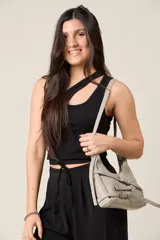 Cartera bandolera de ecocuero texturado color gris claro, con correa ajustable y detalles de hebillas decorativas.