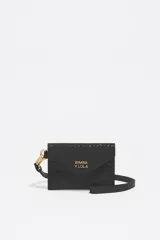 Monedero pequeño de estructura rígida, color negro con acabado brillante (efecto charol o vinilo). Presenta un cierre de solapa con botón a presión y correa de mano/muñeca. El logo metálico dorado de BIMBA Y LOLA está centrado en la solapa.