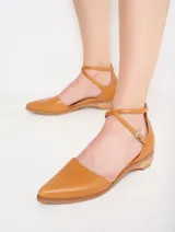 Zapato de cuero color caramelo, con punta fina y tiras cruzadas con hebilla que estilizan el pie y aseguran un calce firme. Su pequeño taco bajo brinda altura justa para el día a día, sin renunciar al confort.