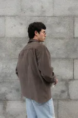 Camisa de corte boxy con estampado de cuadros pequeños en tonos oscuros. Presenta cuello camisero en color negro, cierre frontal con botones, canesú en la parte superior y un bolsillo en el pecho con etiqueta de la marca Kapsul Studio.
