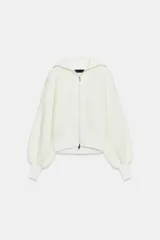 Chaqueta de punto color blanco con cuello subido, cierre frontal de cremallera metálica y mangas largas abullonadas con puños ajustados.