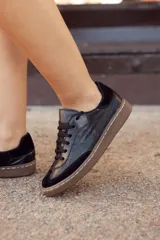 Zapatillas urbanas negras de cuero con detalles en gamuza y suela marrón con costuras blancas.