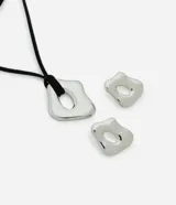 Conjunto de bisutería compuesto por un collar con cordón de gamuza negra y un dije metálico de forma orgánica irregular con un orificio central. Incluye un par de caravanas a juego con el mismo diseño orgánico y orificio central.