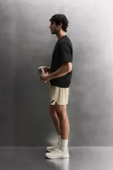 Pantalón corto deportivo color marrón oliva, confeccionado en tejido técnico ligero y elástico, con forro interior. Presenta cintura elástica ajustable con cordón, bolsillos frontales, bolsillo de seguridad trasero con cierre y aberturas laterales en el bajo.