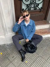 Camisa de denim azul con cuello polo, cierre frontal parcial y dos bolsillos cuadrados en el frente. Presenta un corte holgado y mangas largas.