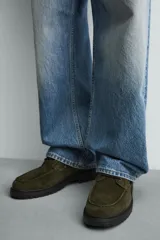 Zapato tipo náutico de hombre, confeccionado en piel con acabado de serraje en color verde oliva. Presenta cordonera con tres pasados, horma redonda y suela track dentada en color negro.
