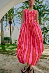 Vestido largo sin mangas con escote en pico y tirantes anchos. Presenta un diseño de rayas verticales en tonos fucsia y rojo, con detalle de falsos botones frontales y cierre de cremallera oculto en la espalda.