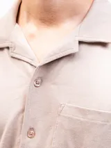 Camisa de manga corta color beige, confeccionada en tejido piqué de algodón, con cuello cubano y un bolsillo de parche en el pecho.