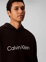 Buzo con capucha Calvin Klein de corte regular, confeccionado en mezcla de algodón regenerado y poliéster reprocesado. Presenta el logo de la marca estampado en el pecho, bolsillo tipo canguro frontal y terminaciones acanaladas en puños y cintura.