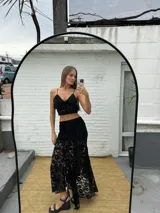 Pollera larga asimétrica color negro, confeccionada en encaje con detalles de terciopelo, de tiro alto y diseño con movimiento y vuelo en el bajo.