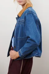 Chaqueta de jean azul con cuello de gamuza color camel, bolsillos delanteros y cierre de botones.