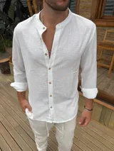 Camisa de cuello mao en color blanco, confeccionada en tela liviana con textura. Presenta cierre frontal con botones de madera y mangas largas con puños arremangados.
