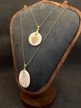 Collar de cadena fina dorada con dije ovalado de cerámica en tono crema, ilustrado con la figura de la Virgen.