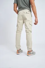Pantalón cargo color beige con ajuste slim, cierre frontal con botón, bolsillos laterales tipo cargo y puños elásticos en los tobillos.