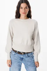 Sweater de punto color crudo con cuello redondo, mangas largas con puños anchos acanalados y cintura también acanalada. Presenta un diseño de silueta holgada y mangas con volumen.