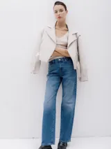 Chaqueta corta estilo biker color beige, confeccionada en piel sintética. Presenta cierre asimétrico frontal, bolsillo con cierre a la vista y bolsillo con solapa, cinturón con hebilla en la cintura.