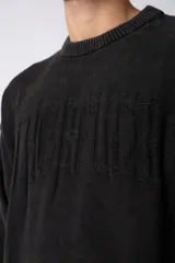 Sweater de punto grueso color negro con efecto gastado, cuello redondo, mangas largas y detalles de roturas en puños y ruedo. Presenta un diseño con letras bordadas al tono en el frente.