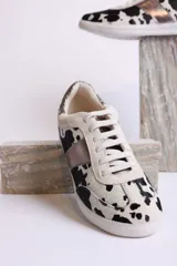 Zapatillas deportivas con estampado animal print de vaca en blanco y negro, con detalles en cuero sintético plateado en los laterales y talón.