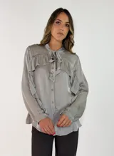 Camisa de satén color naranja óxido, con cuello mao y lazo para anudar. Presenta volados decorativos en el frente y en las mangas, las cuales son largas y terminan en puños abotonados.