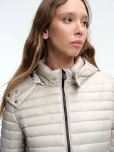 Campera acolchada ultraligera de color blanco, con capucha, cierre frontal de cremallera y bolsillos laterales. Diseño entallado con acabado resistente al viento y la humedad.