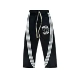 Pantalón de nylon negro con diseño deportivo, presenta tres franjas blancas laterales que se curvan hacia el frente, cordón de ajuste en la cintura y estampado gráfico con la frase 'Mixed Emotion' en la pierna izquierda.