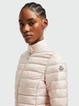 Chaqueta corta acolchada de Moncler, color rosa pálido, con cuello alto, cierre frontal con cremallera y diseño de líneas horizontales.