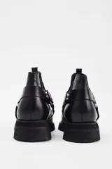 Botineta de cuero vacuno color negro, con diseño estilo western que incluye tiras decorativas, argollas metálicas y tachas plateadas. Cuenta con suela de goma y taco bajo cuadrado.