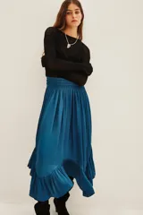 Falda midi de satén en color azul petróleo, con cintura elástica fruncida y diseño asimétrico con volados en el ruedo.