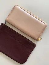 Billetera rectangular de gran tamaño en color rosa metalizado, con cierre perimetral y tirador metálico dorado.