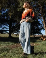 Buzo de tejido de punto con cuello alto y diseño geométrico en zigzag. Presenta una combinación de colores cálidos como naranja, rojo, negro y beige, con puños y cintura acanalados.