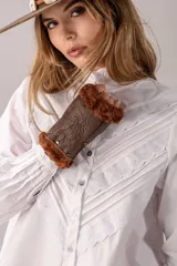 Camisa de algodón color gris azulado, con cuello alto, cierre frontal de botones y mangas largas con puños abotonados. Presenta un diseño con pliegues y detalles de encaje blanco en forma de V en el frente.