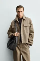 Sobrecamisa de corte boxy fit confeccionada en algodón con estructura canvas y efecto lavado. Presenta cuello solapa, cierre frontal con botones, mangas largas con puños abotonados y bolsillos de plastrón con solapa en el pecho. Incluye detalles bordados a tono en las mangas.