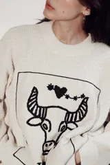 Sweater de punto oversize color crudo, con cuello redondo y diseño bordado a mano en el frente representando al signo Cáncer con un cangrejo, un corazón y una estrella.