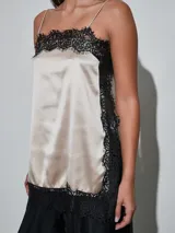 Musculosa de satén color beige claro, con detalles de encaje negro en el escote, los laterales y el ruedo, y tirantes finos.