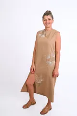 Vestido midi color tostado, sin mangas, con cuello redondo y diseño recto con tajo lateral. Presenta delicados bordados artesanales a mano con motivos florales de dientes de león en tonos blancos y verdes.