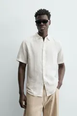 Camisa de lino color beige de corte relajado, con cuello solapa, manga corta y cierre frontal con botones.