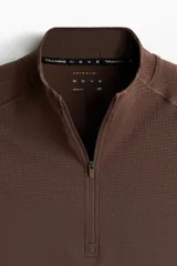 Remera deportiva de manga larga con cuello elevado y medio cierre, de color marrón, con diseño entallado Muscle Fit y detalles de paneles texturizados.