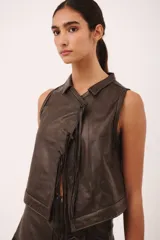 Top sin mangas de cuero color marrón oscuro, con cuello tipo camisa y cierre frontal anudado con tiras de cuero. Presenta pespuntes contrastantes en color claro.