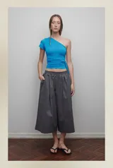 Bermuda gris de corte ancho, con pretina elástica, tiro bajo, bolsillos laterales y cierre lateral.